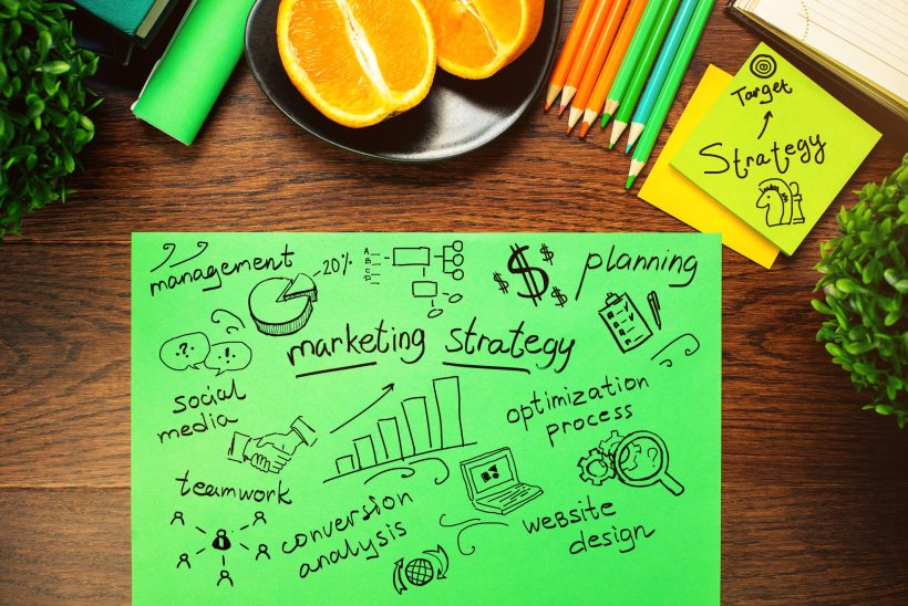 Top view of wooden desktop with decorative plants, orange halves and business sketch on green paper sheet. Strategy concept